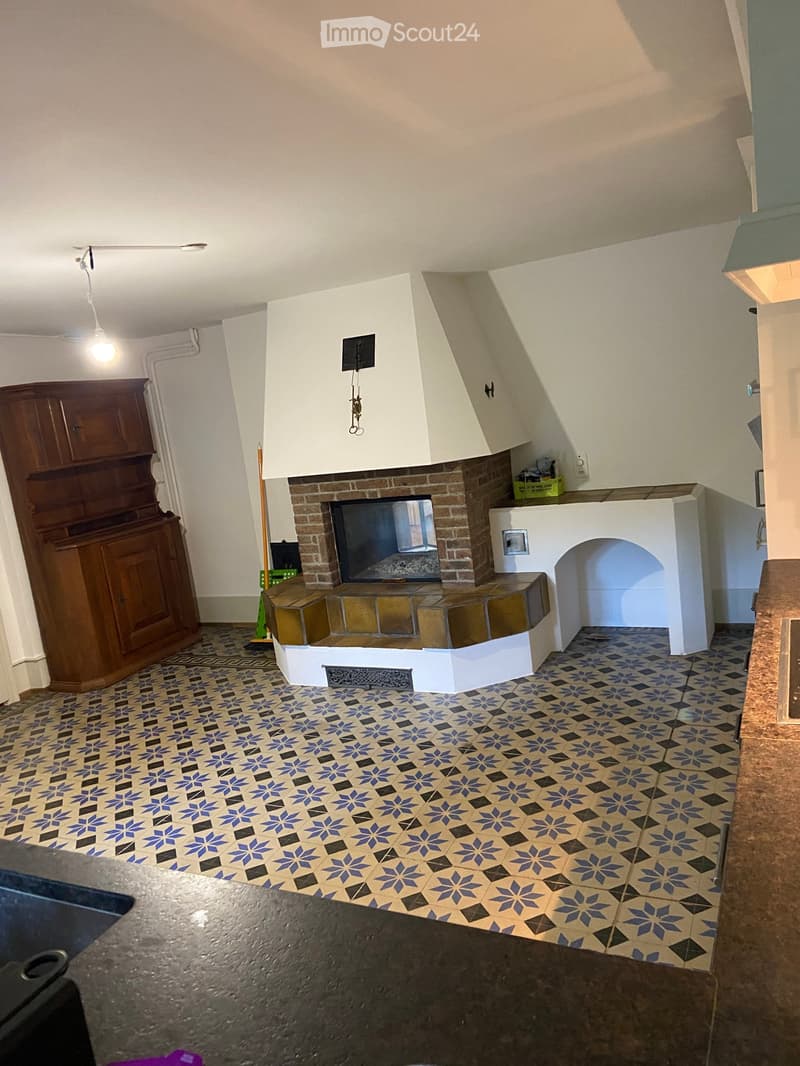 Living room with a brick fireplace, patterned tile floor, wooden cabinet, and hanging light fixture.