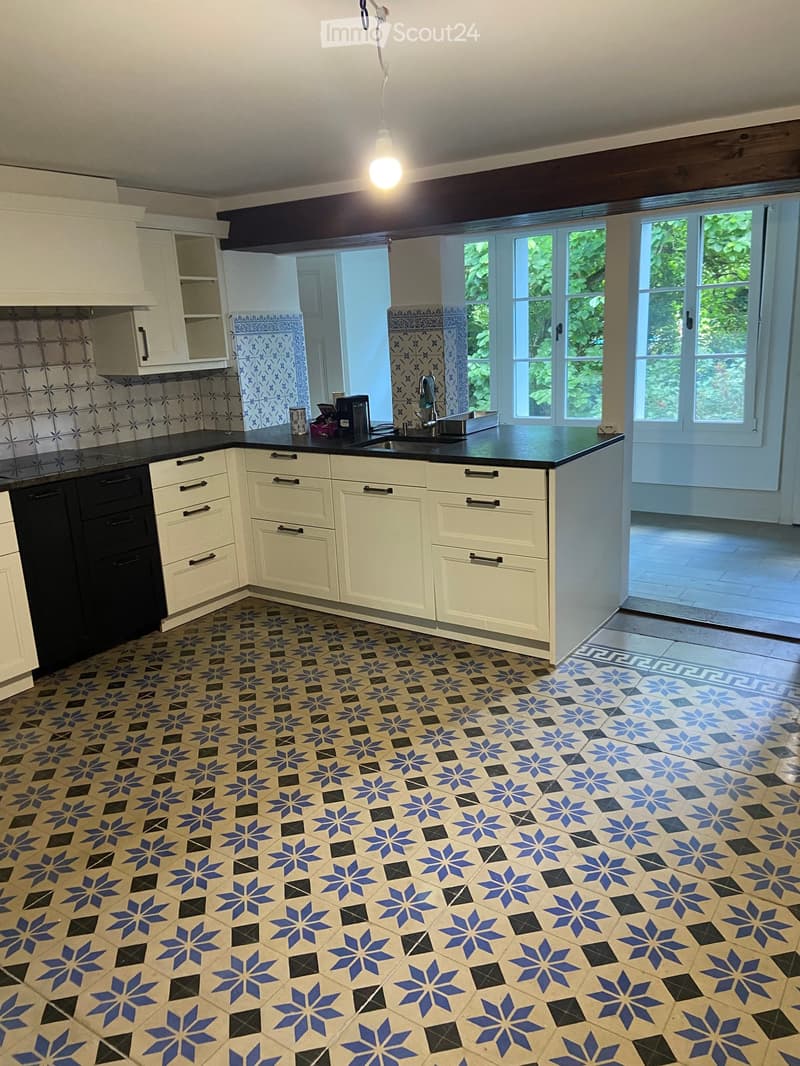 Bright kitchen with white cabinets, black countertops, and patterned tiles. Features a sink, faucet, and a coffee maker on the counter.