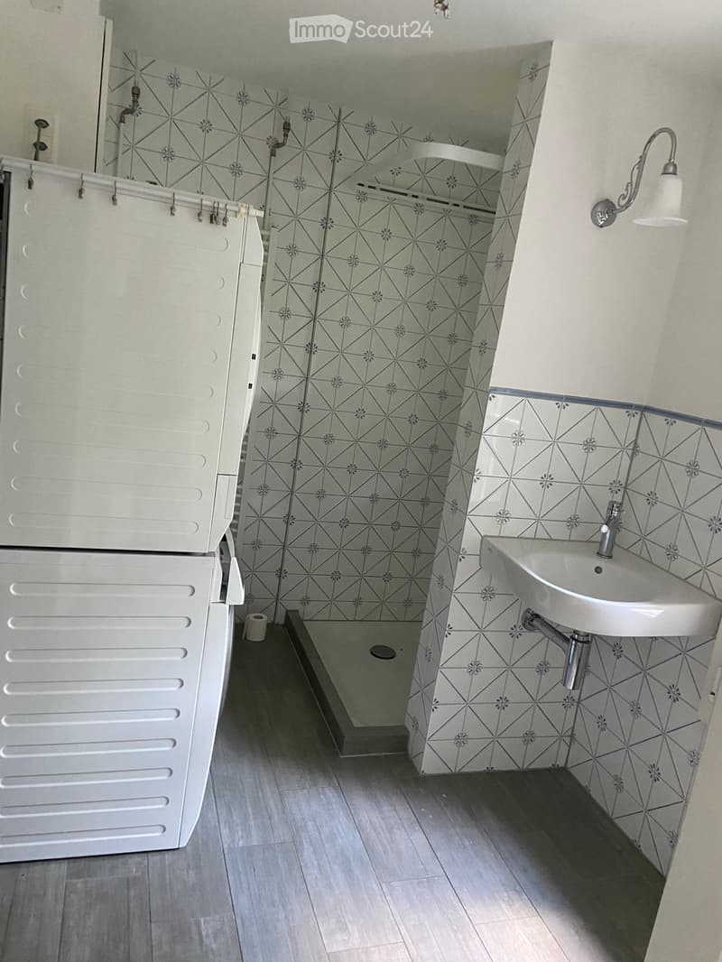 Modern bathroom with grey geometric patterned tiles, white sink, cabinet, and a small shower area.