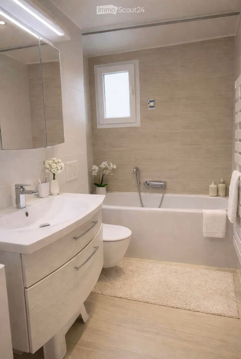Modern bathroom with a white sink, toilet, bathtub, and a small window. Includes a mirror, flower vases, and towels.