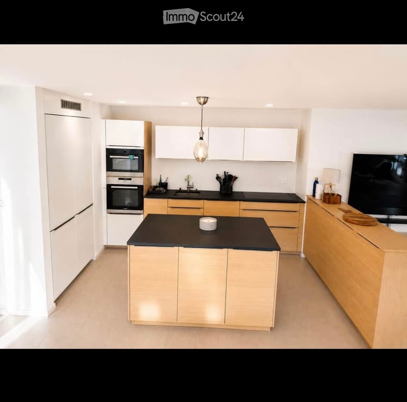 Modern kitchen with white and light wood cabinets, black countertops, stainless steel appliances, and a central island.
