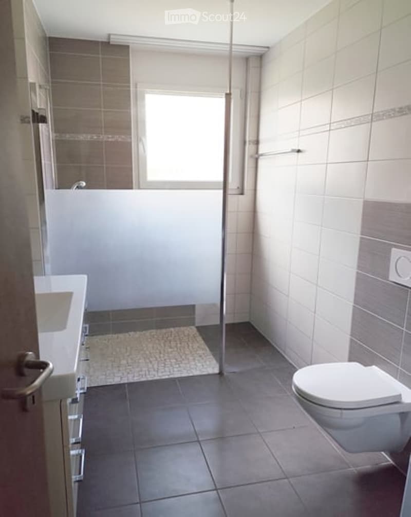 Bathroom with white tiles, white sink, white toilet, glass shower enclosure, window
