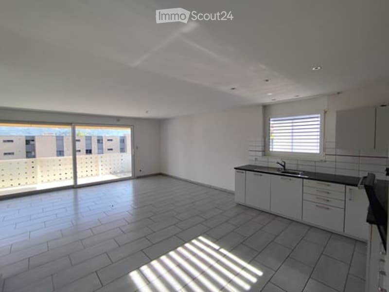 Unfurnished Room. An empty room with white tiles, white walls, and a glass door leading to a balcony. There is a sink and cabinets in the kitchen area.