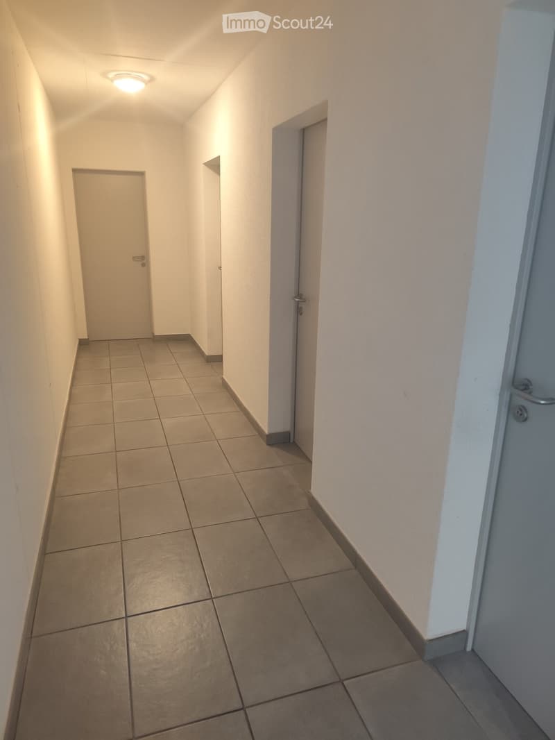 Empty hallway with tiled floor and white walls, two doors visible, one of which is closed and the other is open