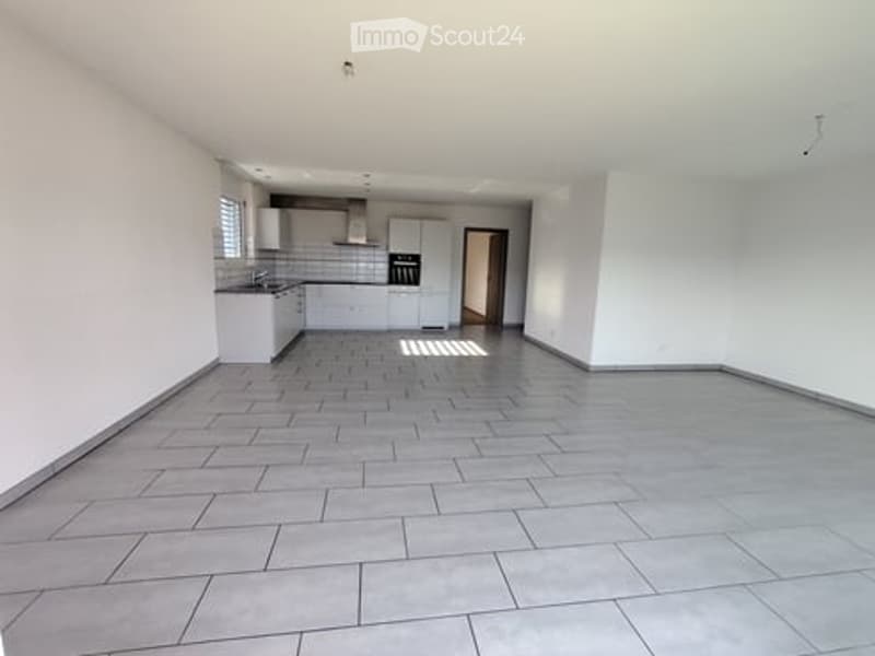 Unfurnished Room. Empty room with white walls, gray tiled floor, and a kitchen area with cabinets and a sink.