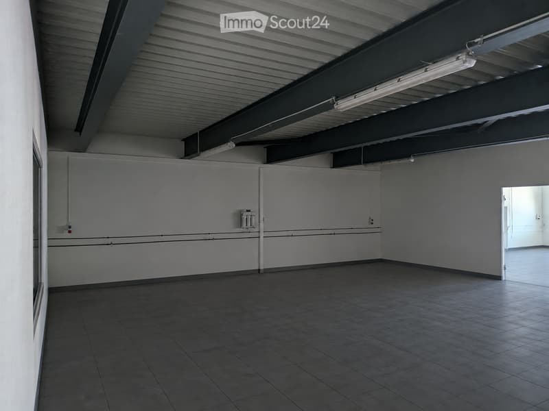 Empty room with tiled floor, white walls, and industrial-style ceiling with exposed beams and fluorescent lighting. No furniture or equipment present.
