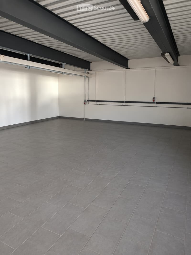 Empty room with grey tiled floor and white walls, featuring exposed metal beams and lighting fixtures on the ceiling.