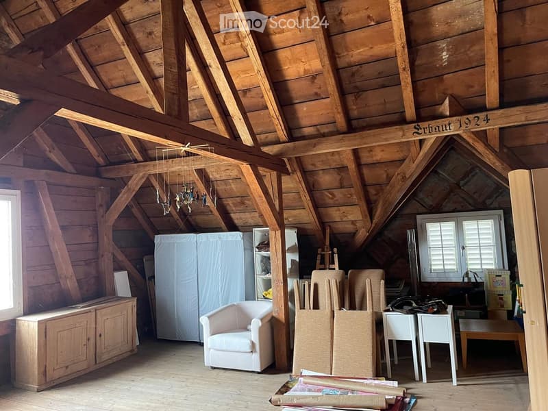 Loft-style room with wooden beams, exposed ceiling, white sofa, wooden cabinet, and various furniture pieces.