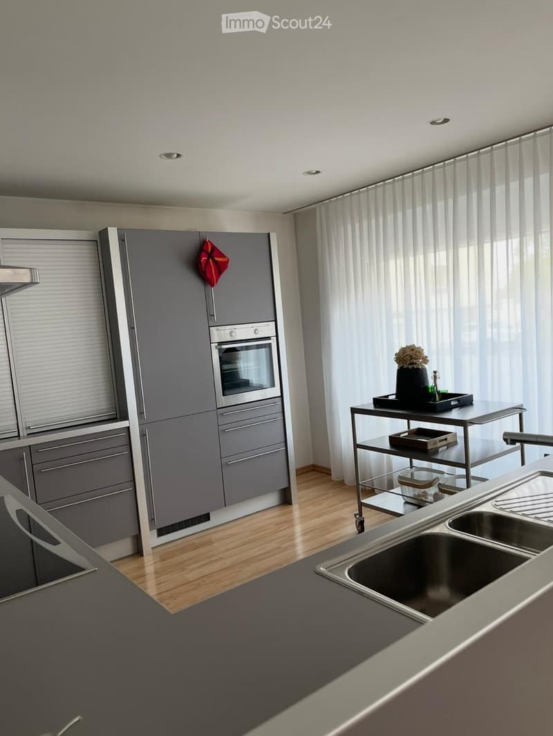 Modern kitchen with grey cabinets, stainless steel appliances, wooden flooring, and a small table with a vase and tray.