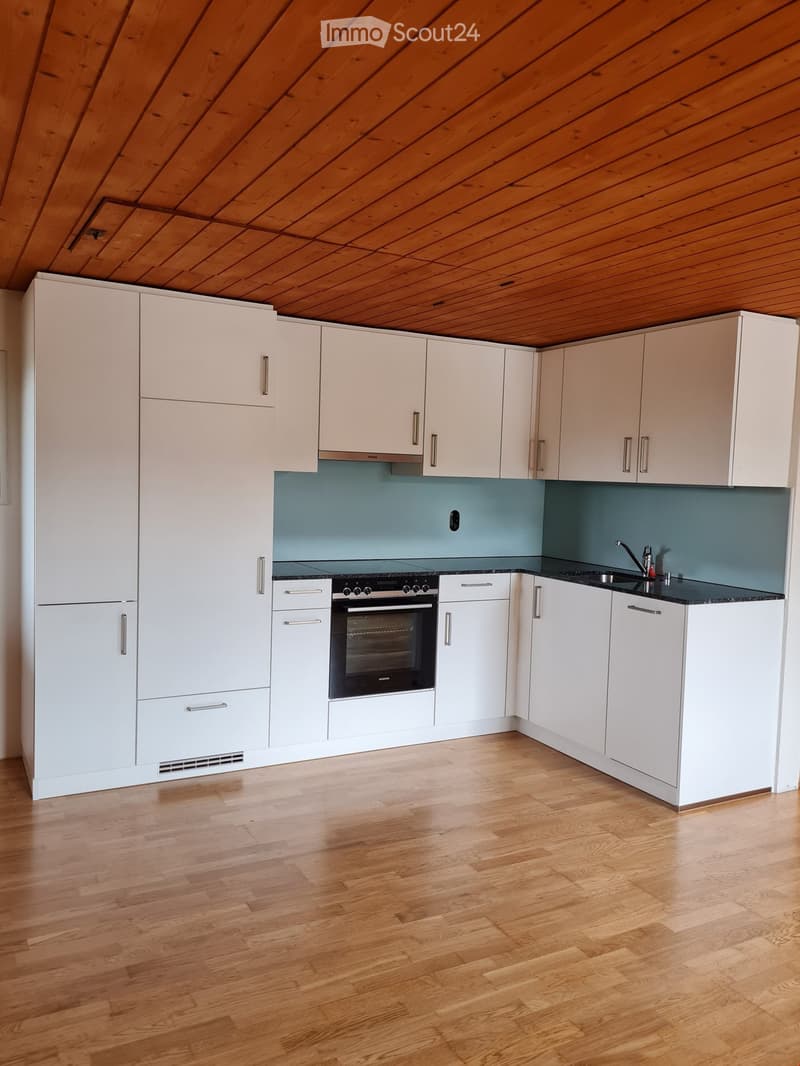 Modern kitchen with white cabinets, wooden flooring, and a built-in oven. The backsplash is a light blue color, and the sink features a modern faucet.
