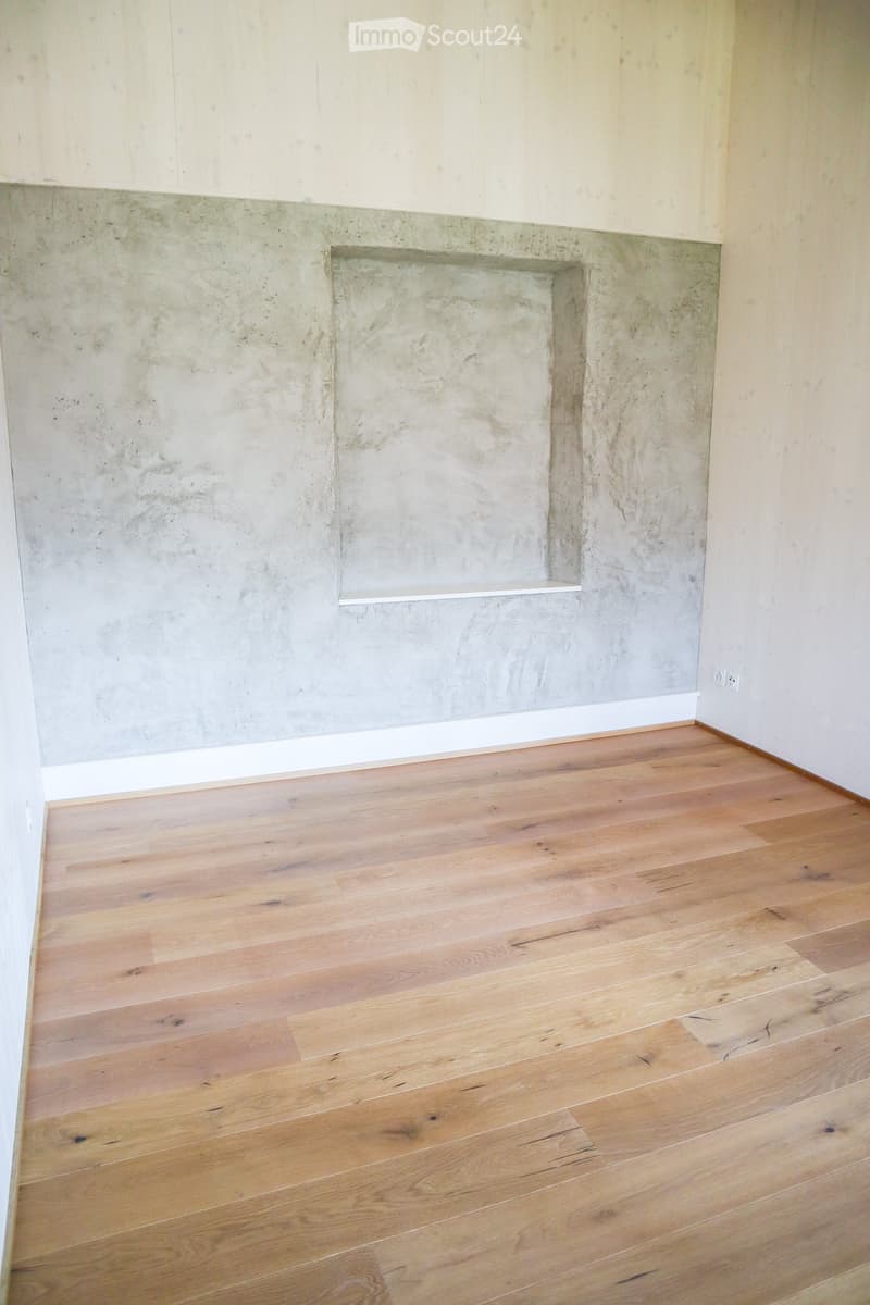 Empty room with light wooden flooring and a built-in concrete fireplace with a white shelf above it.