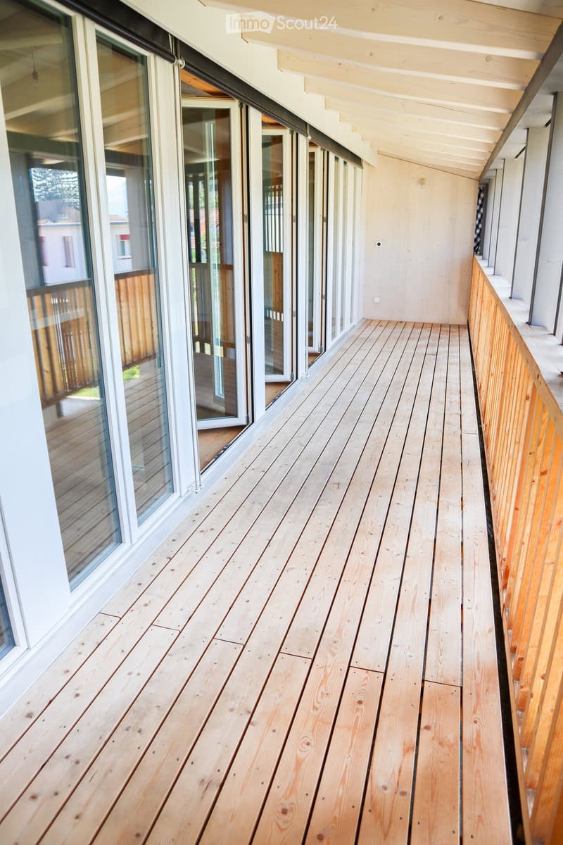 Wooden deck with white railings, large glass doors leading to the interior, and a view of the surrounding area.