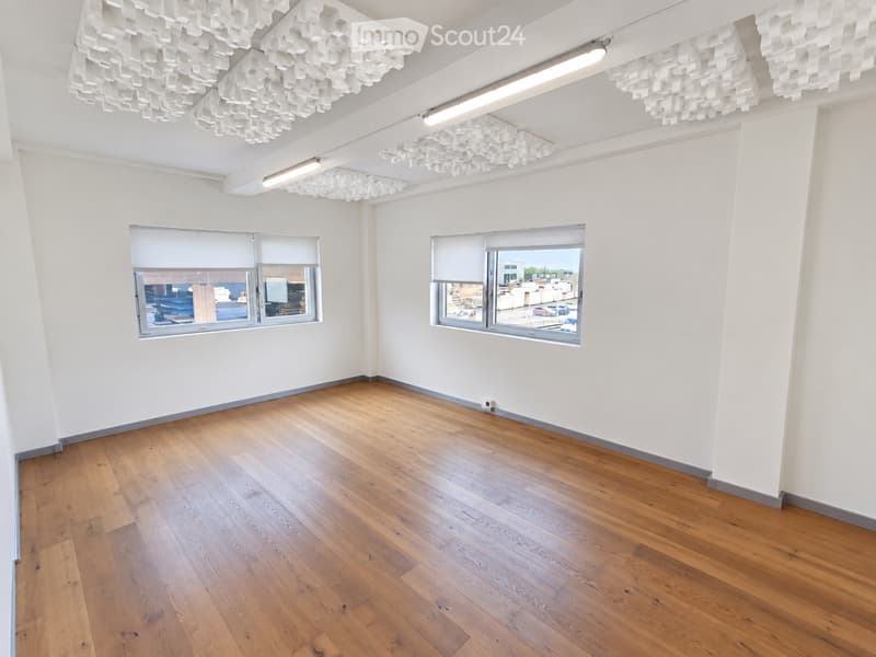Empty room with wooden flooring, white walls, large windows with blinds, and modern geometric light fixtures on the ceiling.