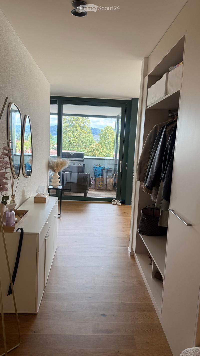 Modern hallway with wooden flooring, built-in storage unit, coat rack, and a view to a balcony area with outdoor furniture.