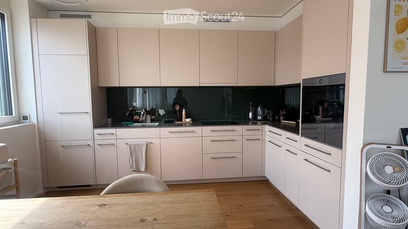 Modern kitchen with light-colored cabinets, stainless steel appliances, and a wooden dining table with chairs.