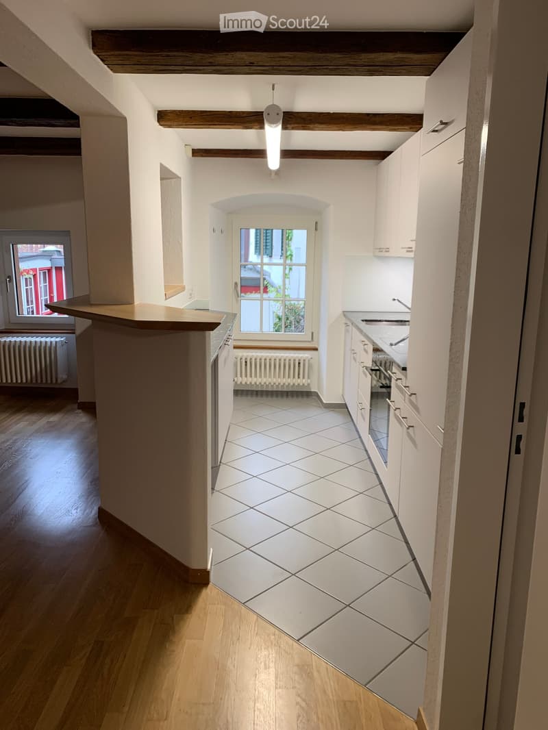 Modern kitchen with white cabinets, tiled floor, wooden countertop, and natural light from windows.