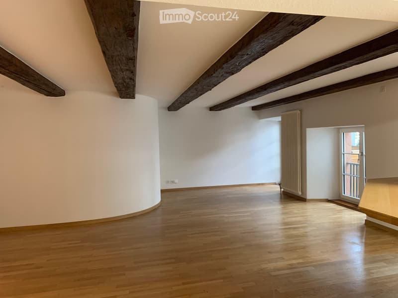 Empty room with wooden flooring, white walls, exposed wooden beams on the ceiling, and a radiator on one wall.