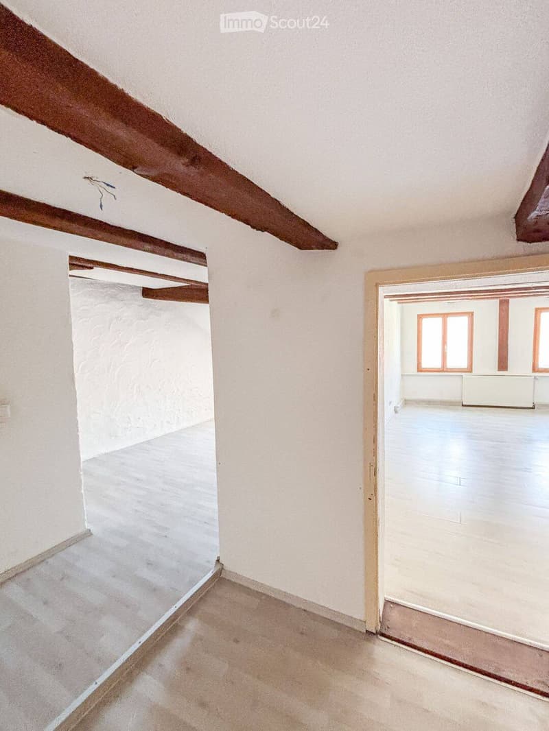 Empty attic space with exposed wooden beams, white walls, and concrete floor. No furniture or equipment present.