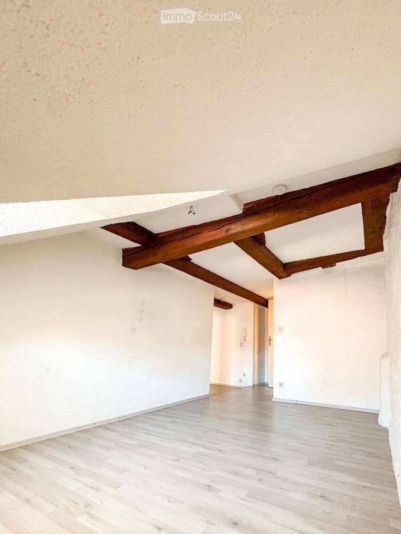 Empty room with light wooden flooring, white walls, and exposed wooden beams on the ceiling. No furniture or equipment is present.
