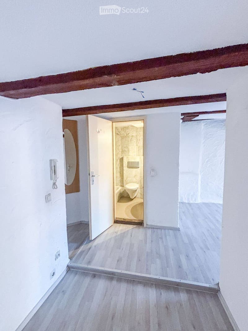 Empty room with white walls, wooden floor, and an open doorway leading to a small bathroom with a toilet and bathtub.