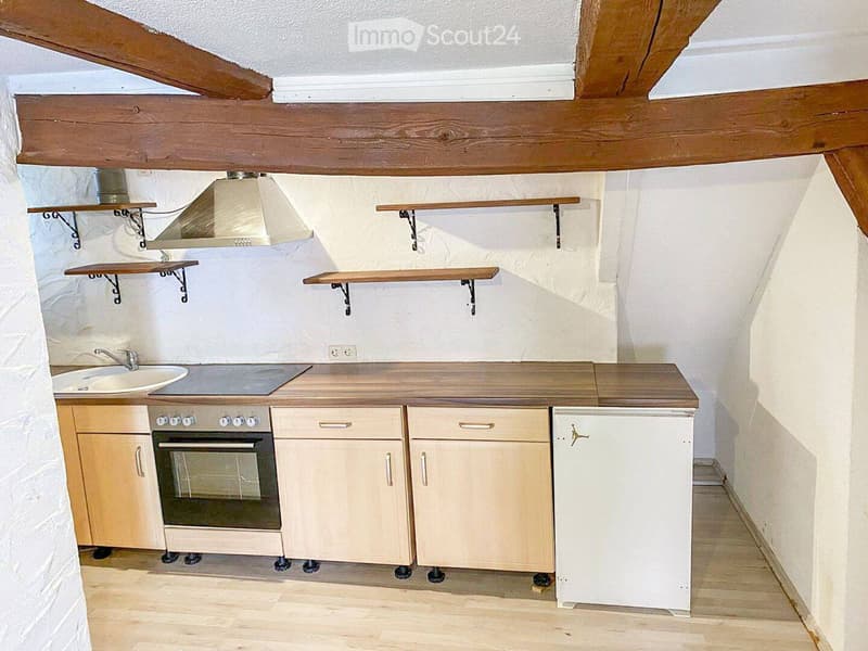 Compact kitchen with wooden cabinets, a sink, an oven, a refrigerator, and wooden shelves mounted on the walls.
