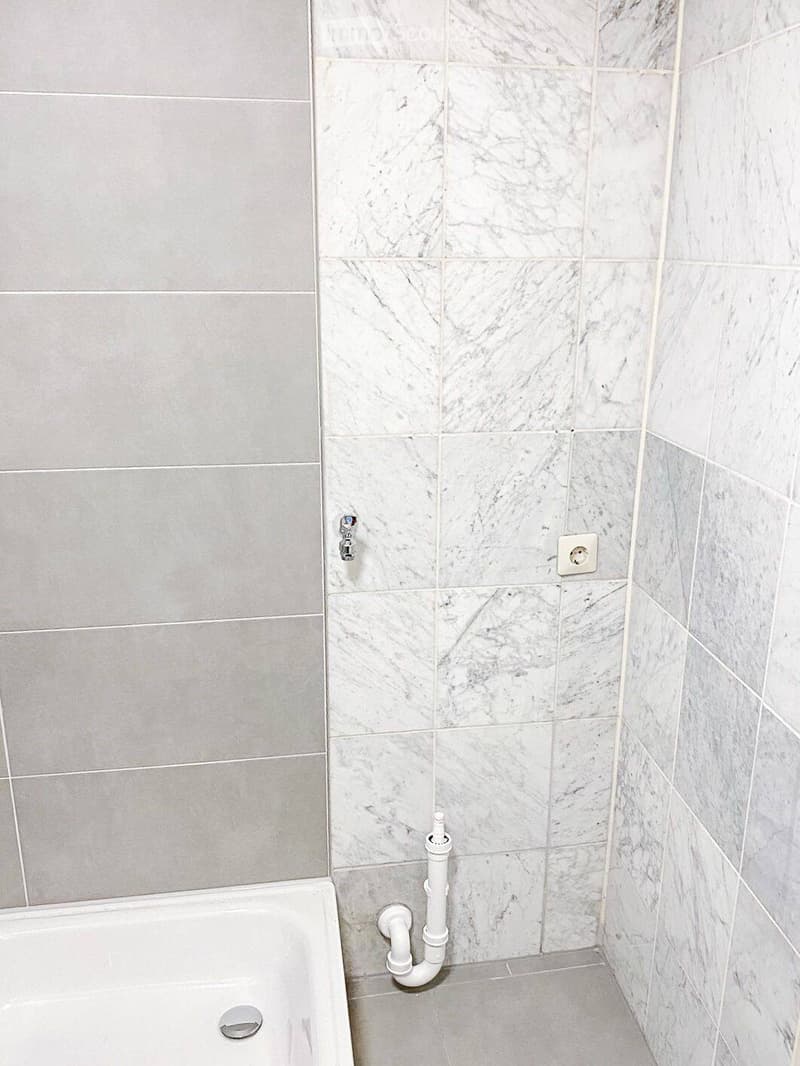 Bathroom with marble tiles, a bathtub, and visible plumbing pipes.