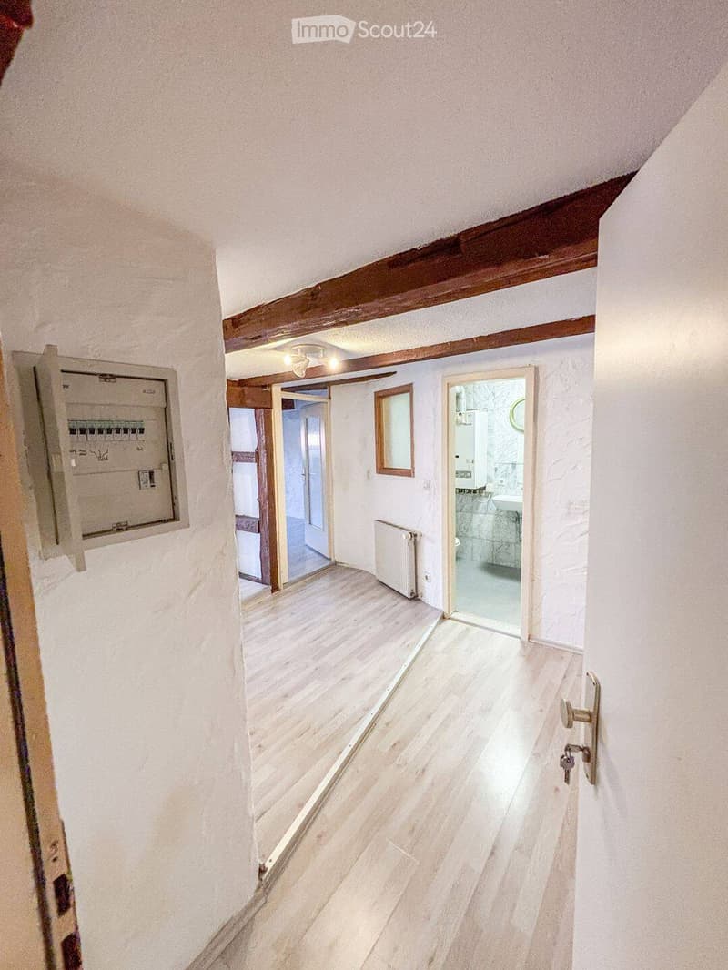 Empty hallway with wooden flooring, white walls, exposed wooden beams, and doors leading to other rooms.