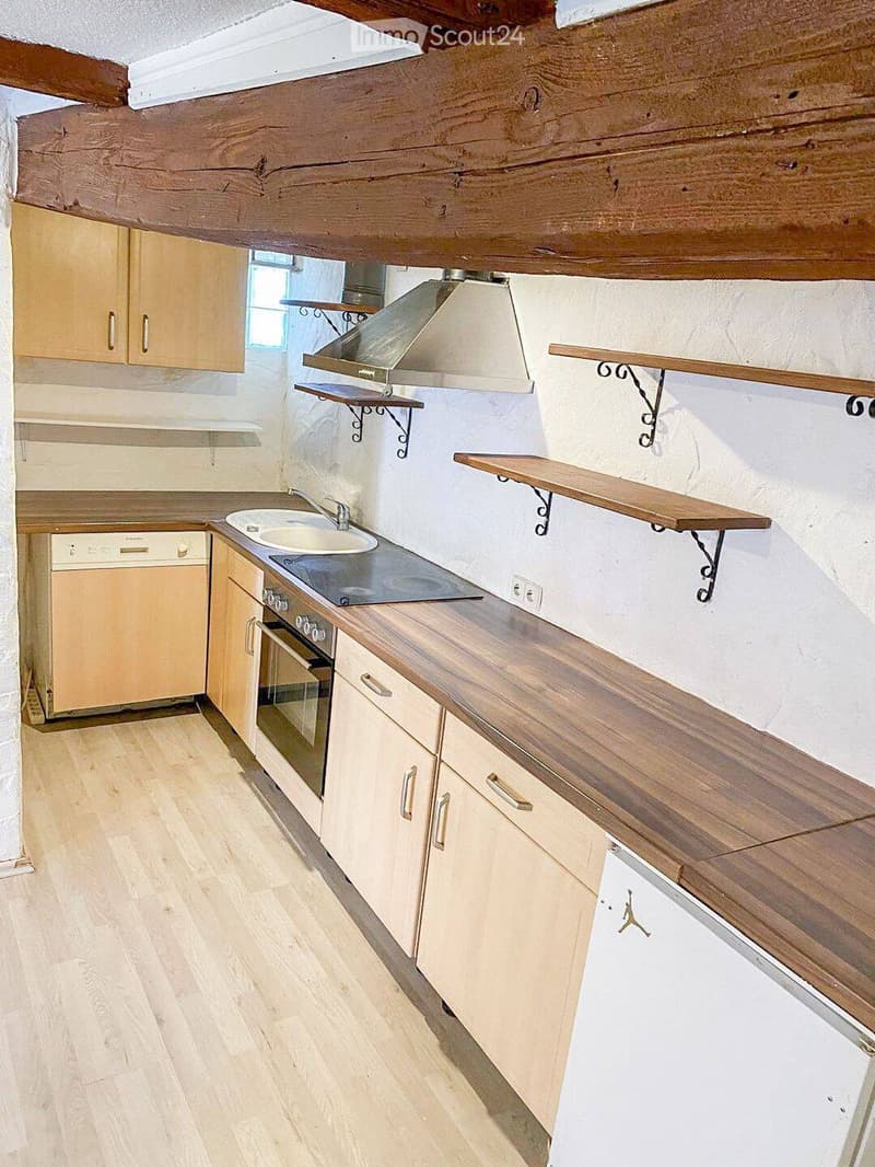Bright kitchen with wooden countertops, cabinets, sink, oven, and dishwasher. Exposed wooden beams on the ceiling and wooden shelves on the walls.