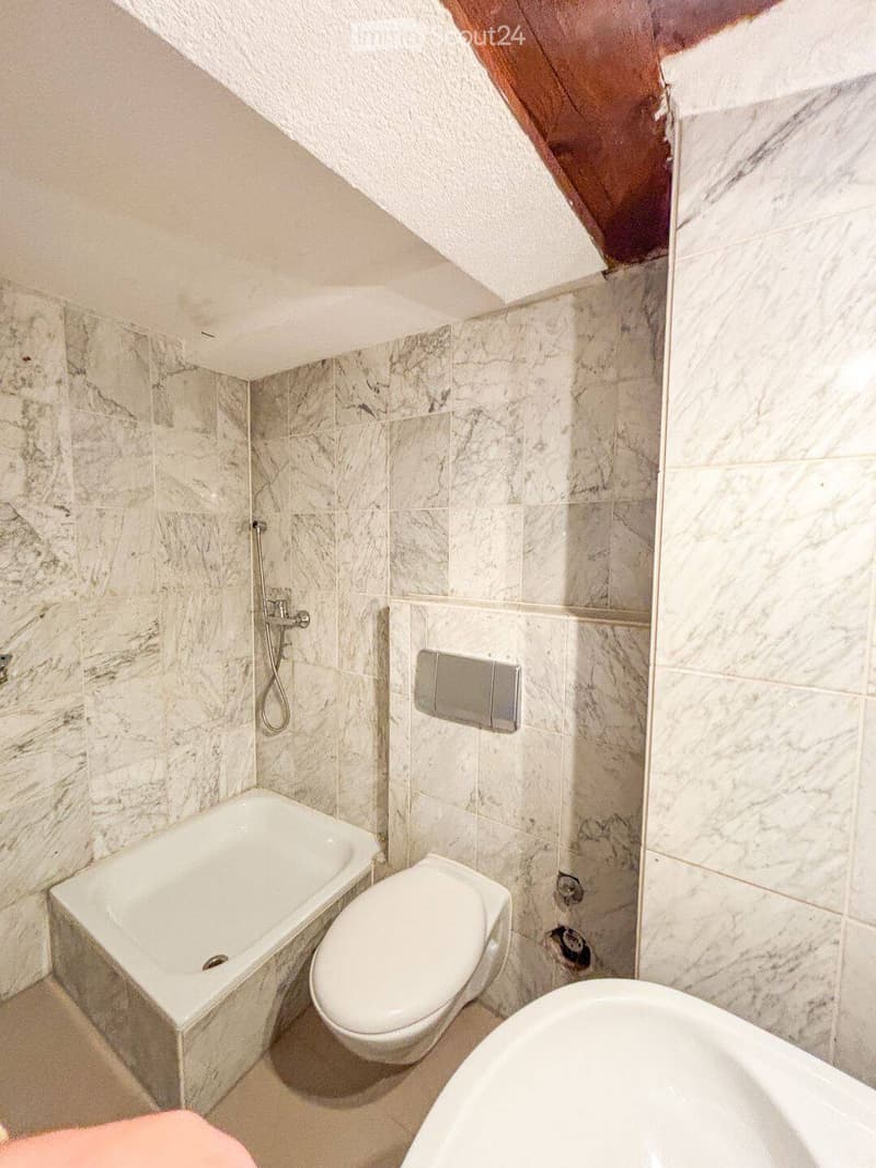 Modern bathroom with marble tiles, a bathtub, toilet, and a showerhead.
