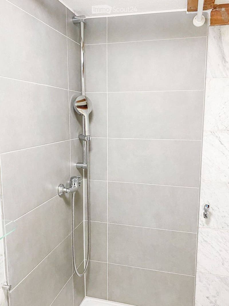 Modern bathroom with grey tiled walls, a handheld showerhead, and a chrome faucet.