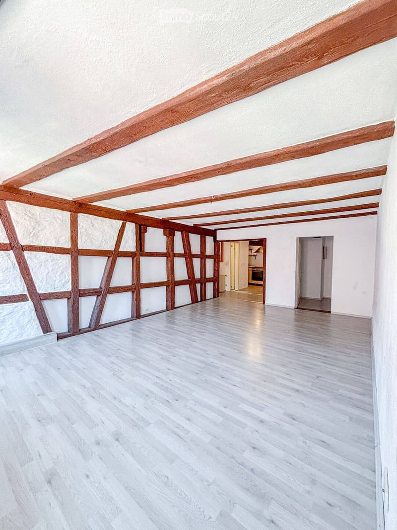 Empty room with wooden beams on the ceiling, white walls, and light wooden flooring. No furniture or equipment is present.