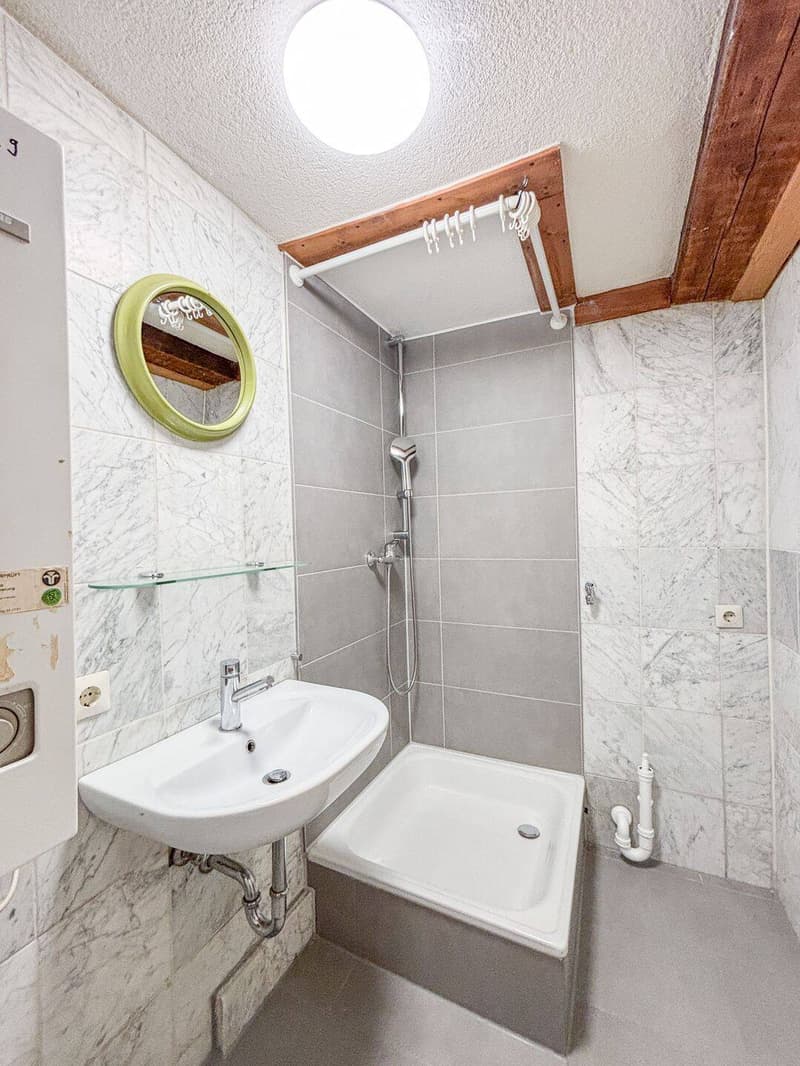 Modern bathroom with a white sink, round mirror, glass shelf, and a small shower area with a modern showerhead.