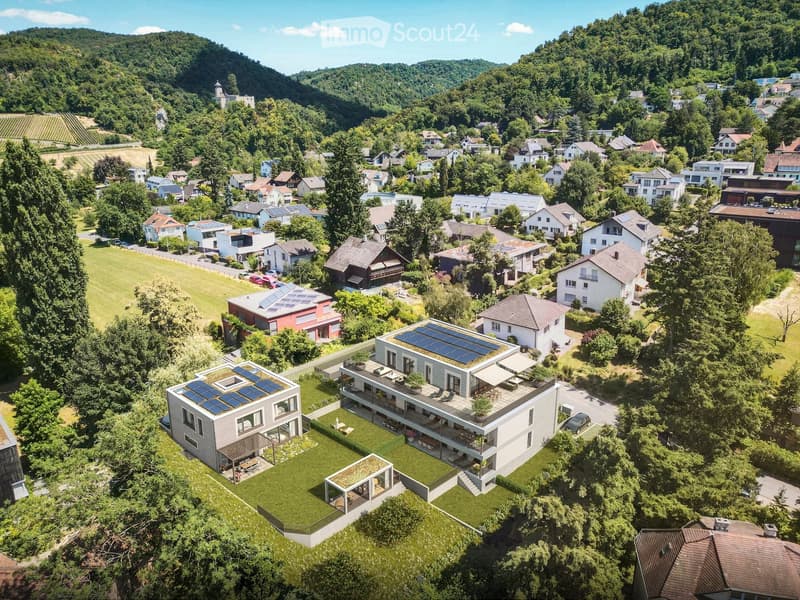 Aerial view of a residential area with multiple houses, surrounded by greenery and hills. Houses feature modern designs with solar panels on rooftops, and there are well-maintained lawns and outdoor seating areas.