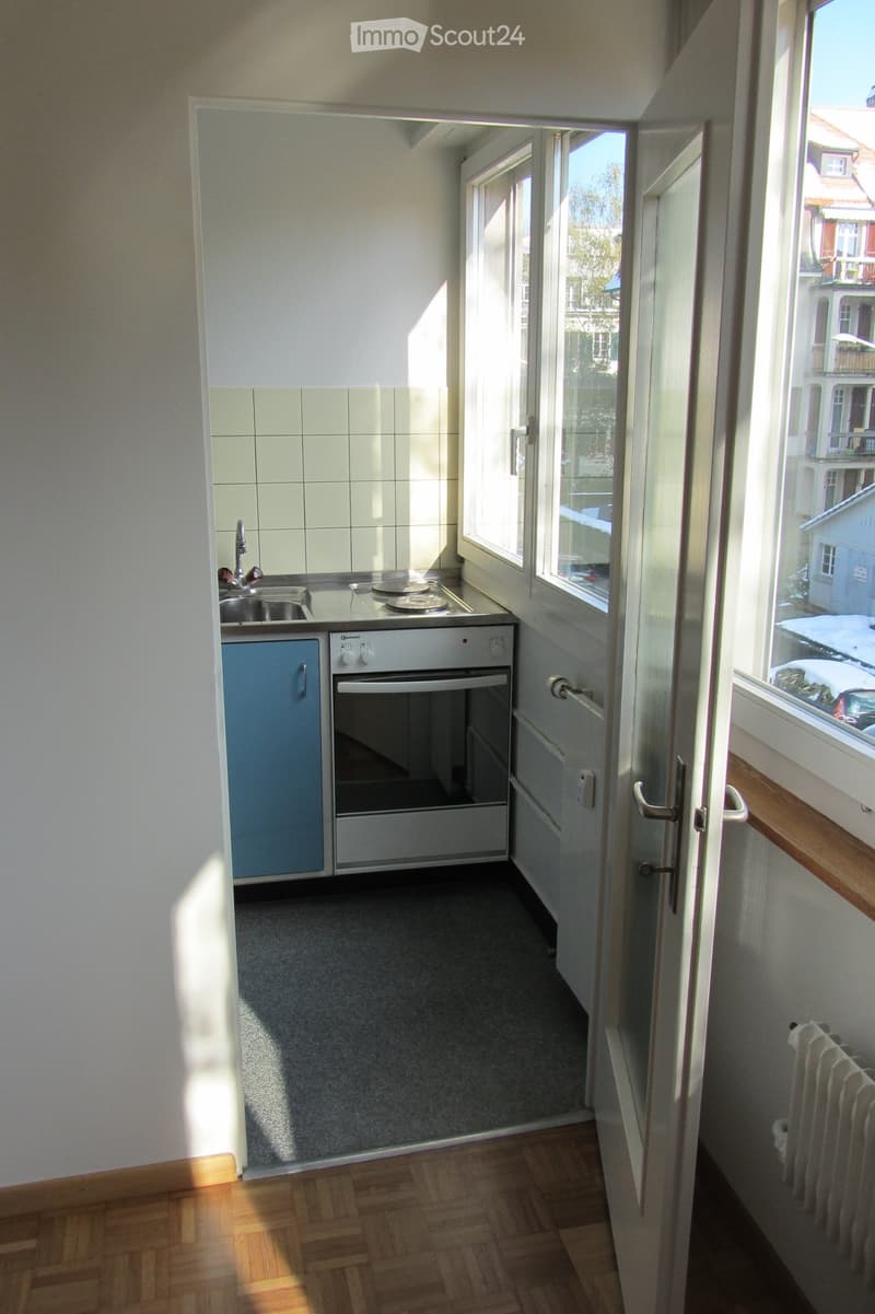 Compact kitchen with white tiled backsplash, grey countertop, sink, faucet, and built-in oven. Light blue cabinet and wooden flooring visible.