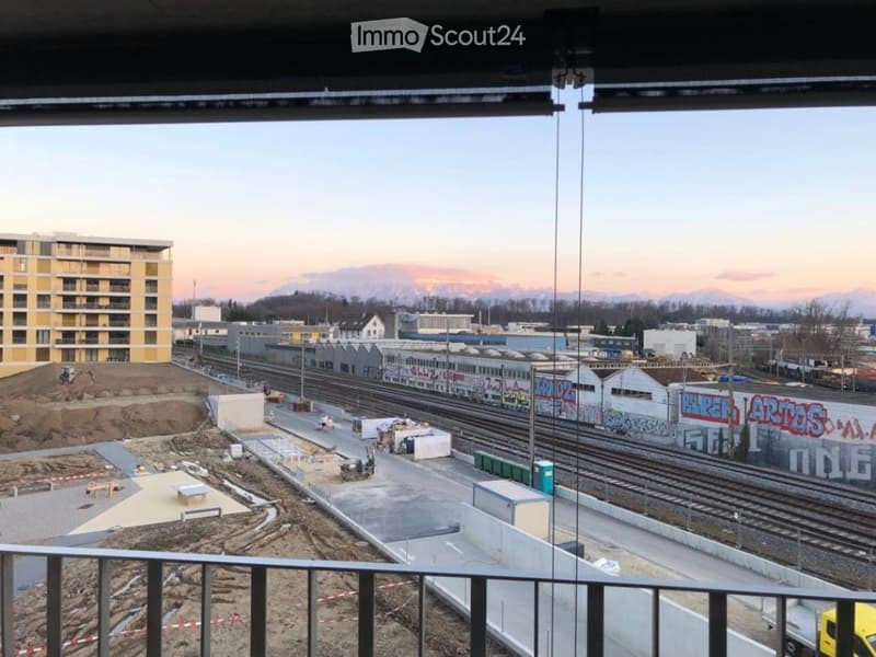 Balcony overlooking a construction site with railway tracks, buildings, and distant mountains.