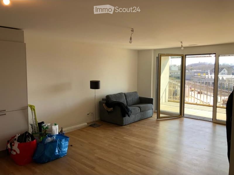 Modern living room with wooden flooring, large sliding glass doors leading to a balcony, a grey sofa, and a floor lamp.