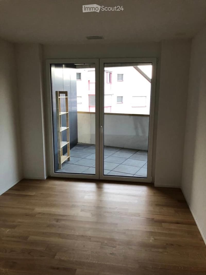 Empty room with wooden flooring and large sliding glass doors leading to a tiled balcony area.