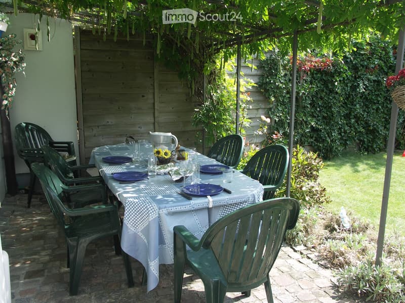 Outdoor dining area with a table set for a meal, surrounded by greenery and wooden fencing.