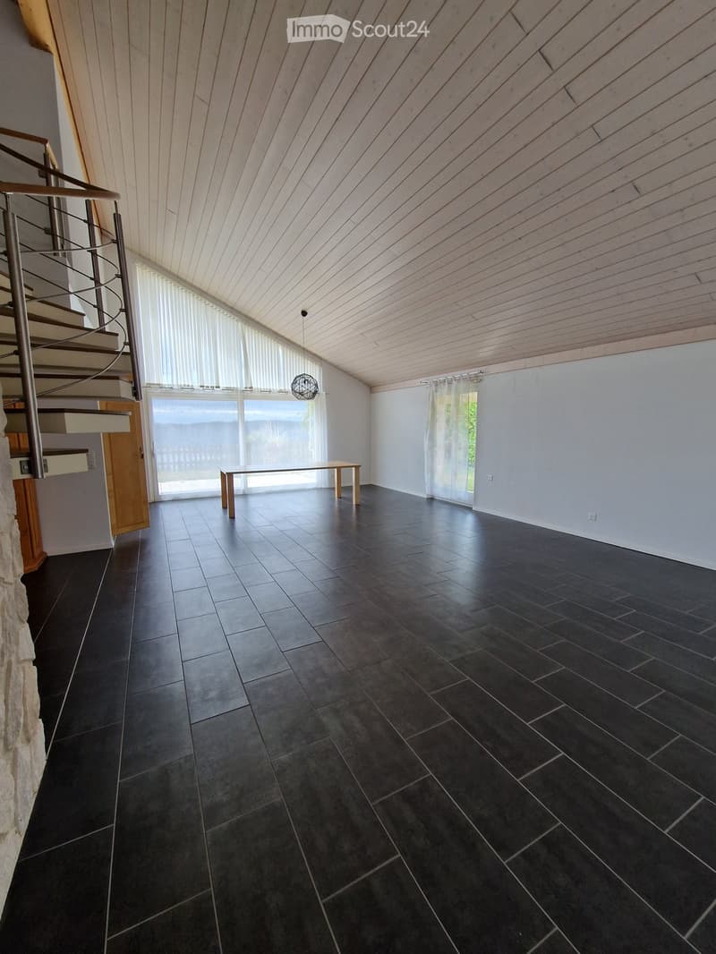 Empty room with dark tiled floor, wooden ceiling, large windows, and a small table near the window.