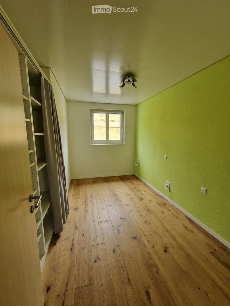 Empty room with light green walls, wooden floor, window, and built-in shelving unit.