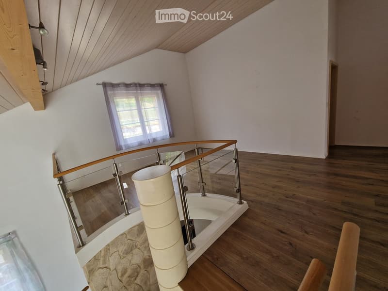Modern hallway with wooden flooring, glass railing, and a stone pillar. Features a window with sheer curtains and recessed lighting.