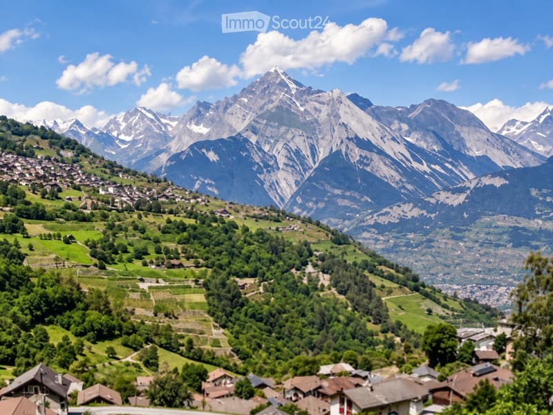 A picturesque alpine village nestled in a lush green valley, surrounded by towering snow-capped mountains under a clear blue sky.
