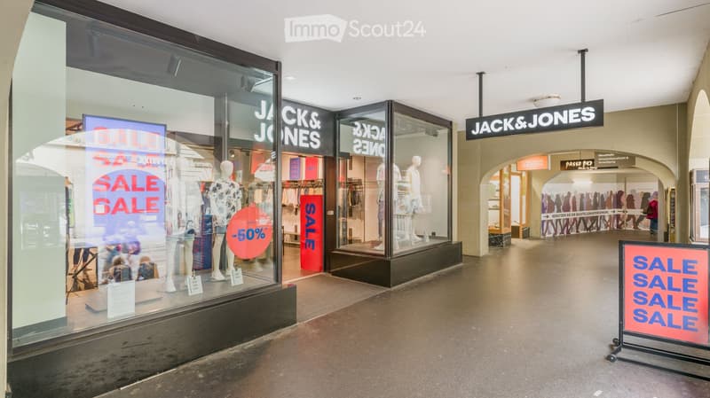 Shopping mall corridor with a Jack & Jones store, visible mannequins in the window, clothing racks inside, and multiple sale signs.