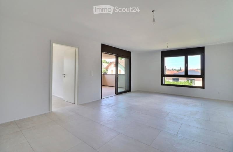 Empty room with white walls, tiled floor, large window, and sliding glass door leading to a balcony.