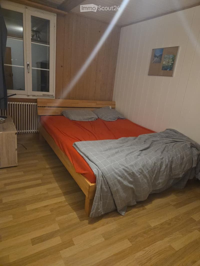 Cozy bedroom with wooden flooring, a single bed with red and grey bedding, a nightstand, radiator, and a picture frame on the wall.