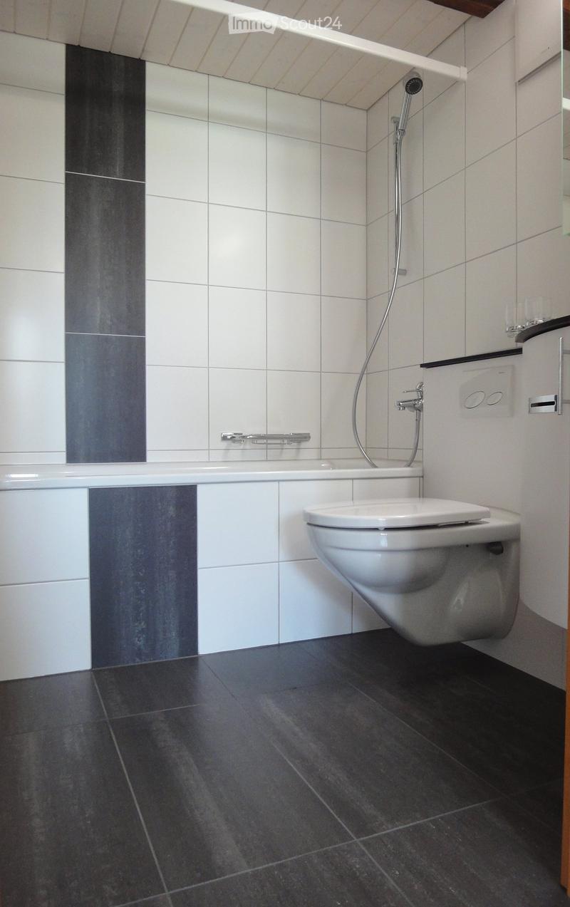 Modern bathroom with white tiles, dark grey floor tiles, a toilet, bathtub, and a showerhead with a handheld hose.