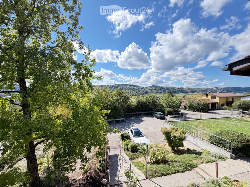 Balcony view showing a landscaped garden area with a parking lot, stairs, and a scenic valley view.
