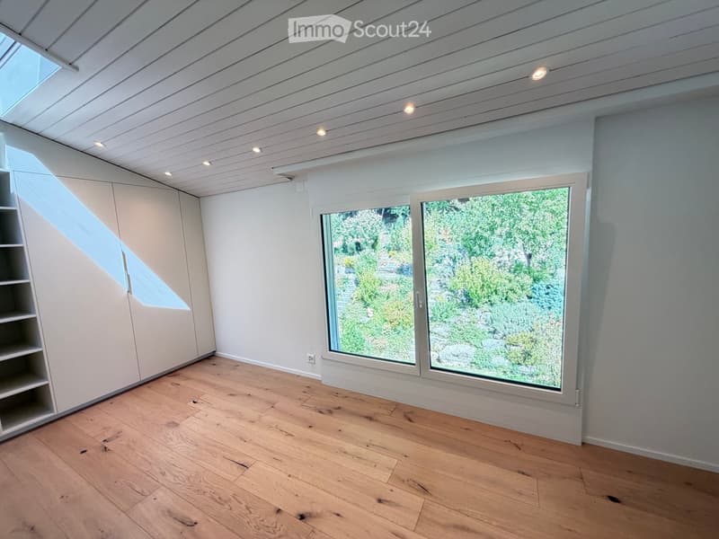 Empty room with wooden flooring, white walls, large windows, and built-in shelving unit.