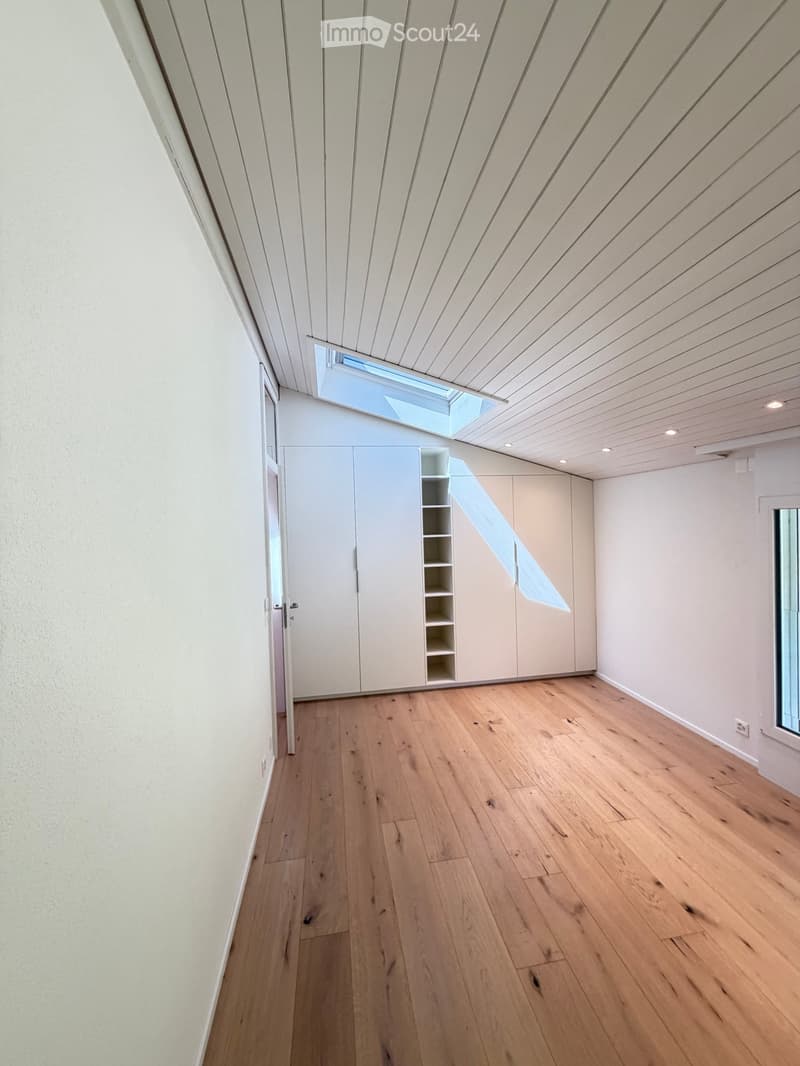 Empty room with light wooden flooring, white walls, built-in closet with shelves, and a skylight above the door.