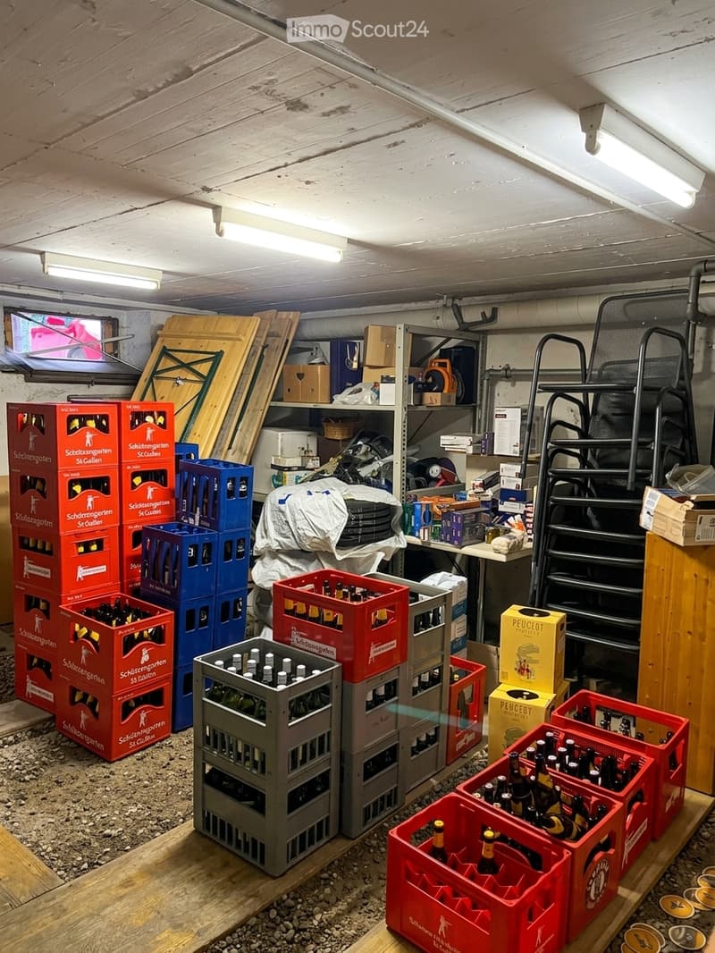 A storage area with shelves, tables, chairs, and numerous crates filled with bottles and boxes.